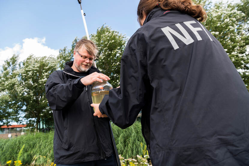 Twee onderzoekers houden een pot met water vast. Eentje draait een rode deksel op de pot.