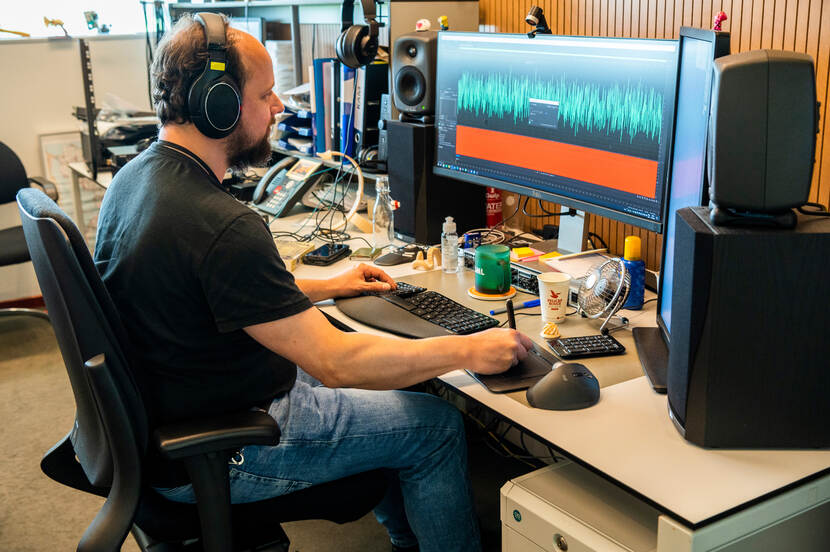 Man met koptelefoon op kijkt naar beeldscherm waar geluidsgolven op te zien zijn