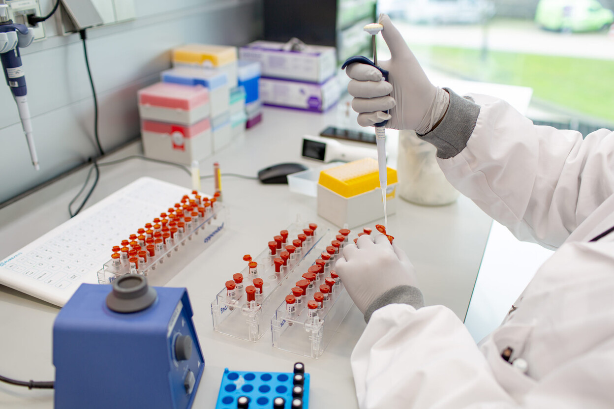 Onderzoeker met pipet in hand aan tafel met rekjes buizen