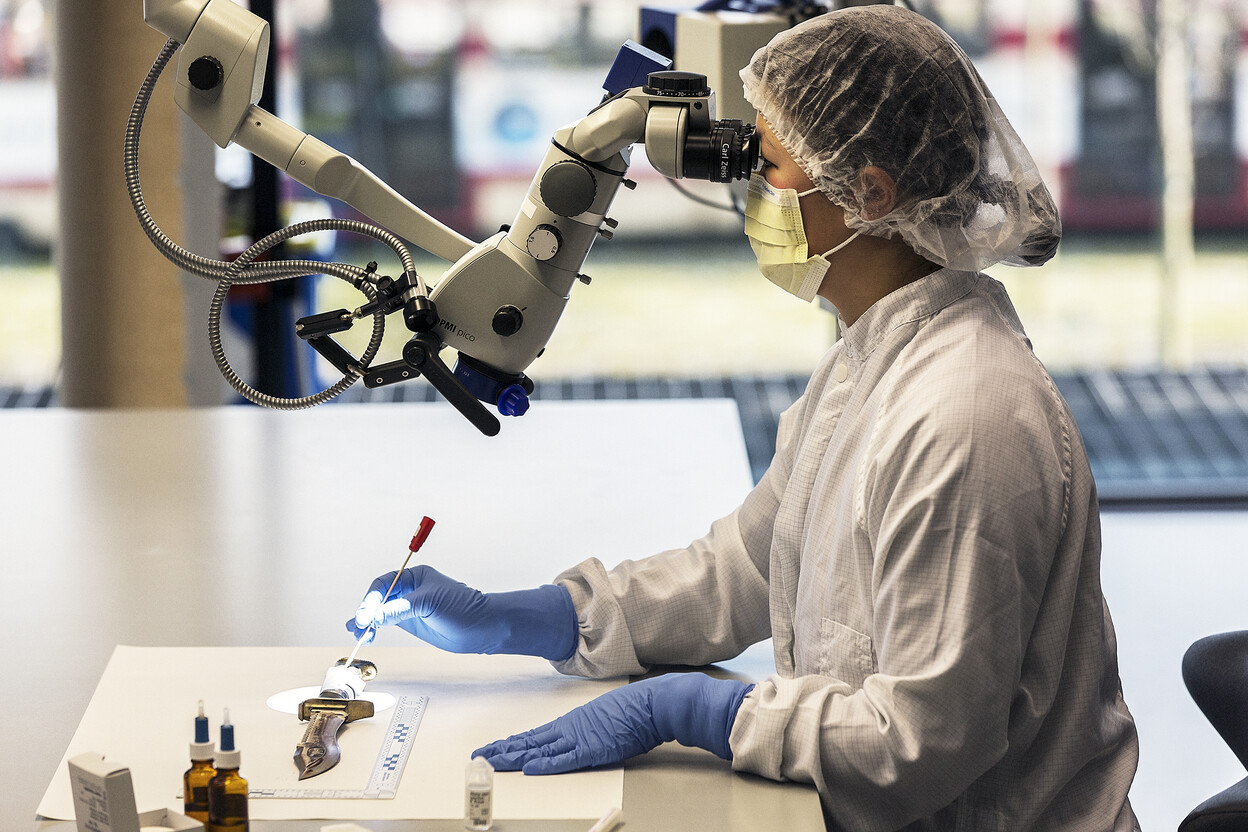 Onderzoeker kijkt door microscoop en gebruikt een wattenstaafje om DNA-sporen te zoeken op een mes