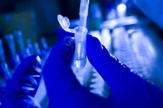 Onderzoeker houdt tube vast voor DNA onderzoek