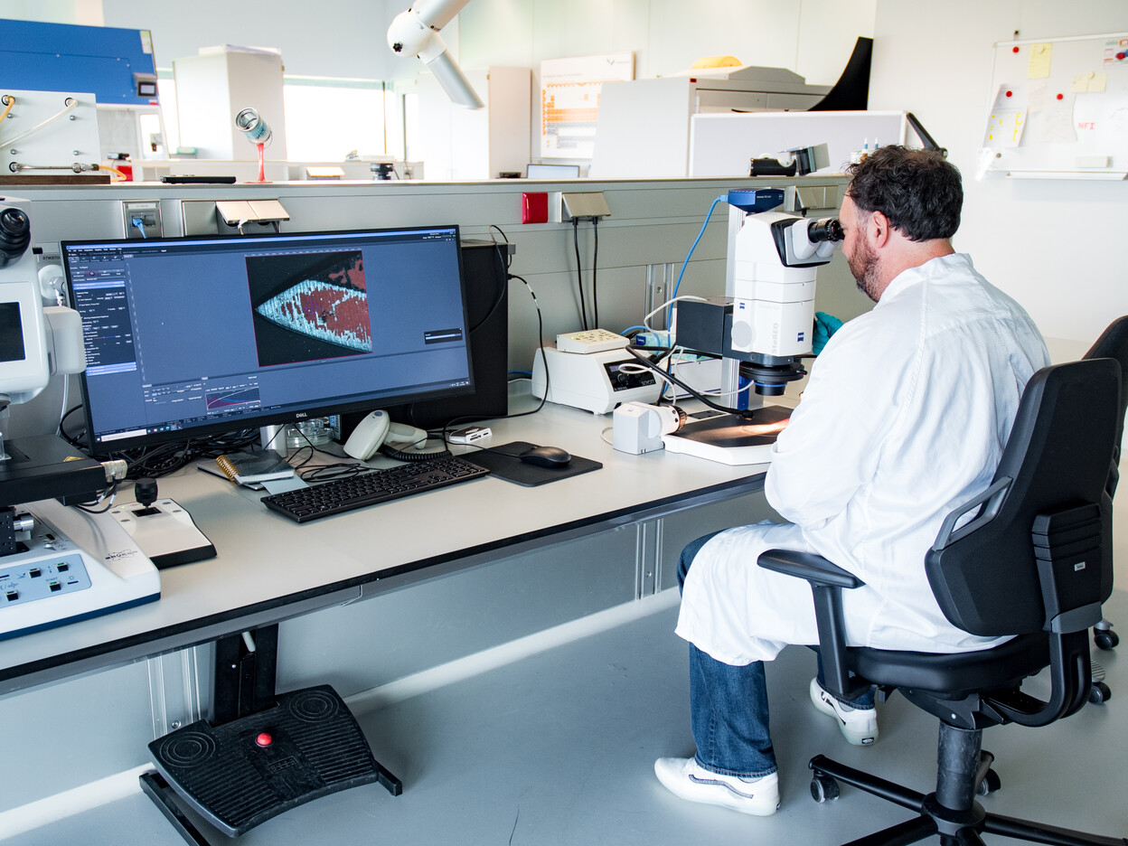Deskundige Microsporen en Materialen Peter Zoon onderzoekt mes met een microscoop