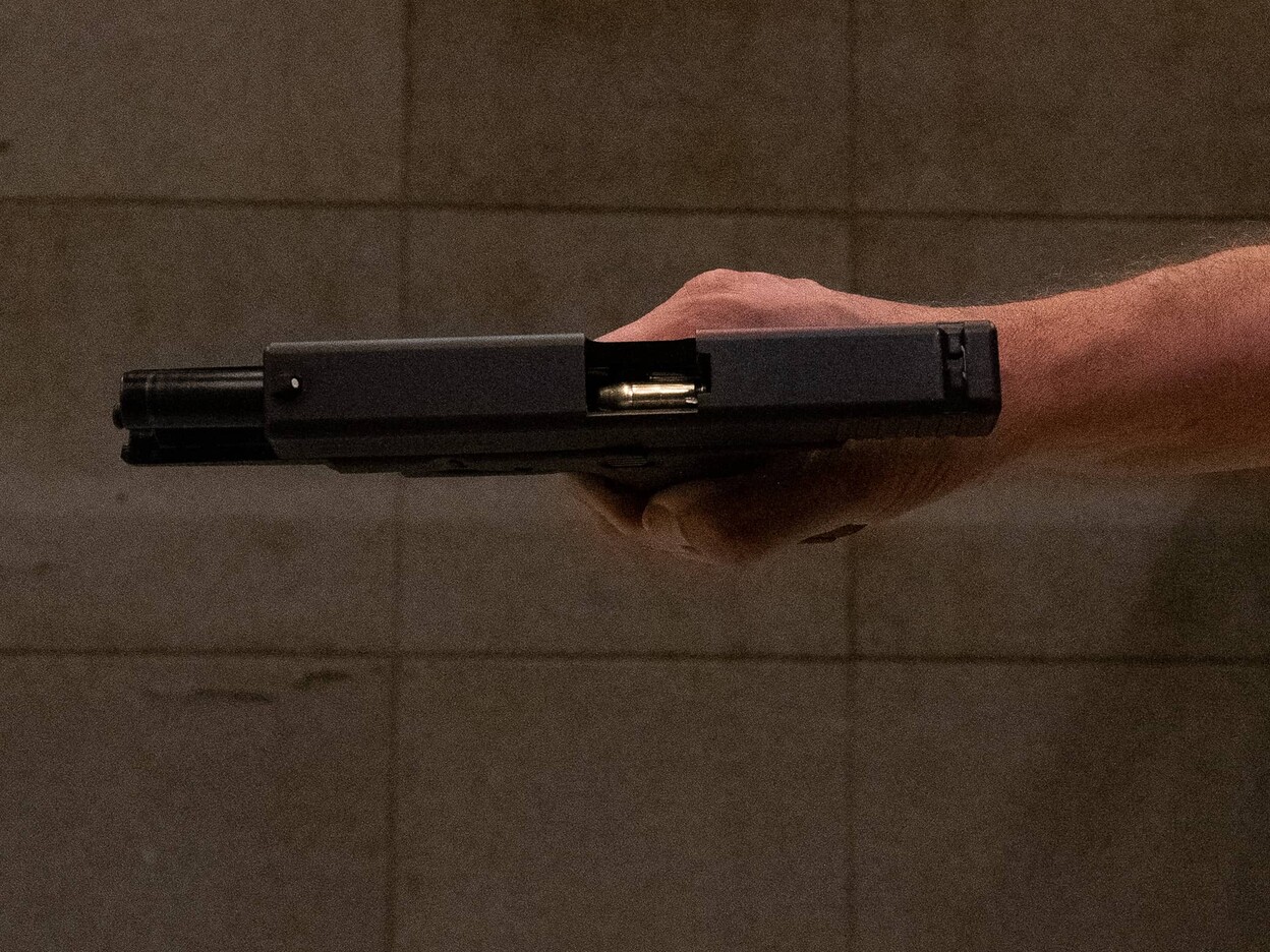 Deskundige houdt een geladen handvuurwapen met een open slede zijwaarts vast