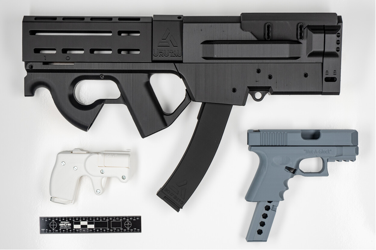 Drie 3D geprinte vuurwapens van verschillende grootte met liniaal op witte tafel