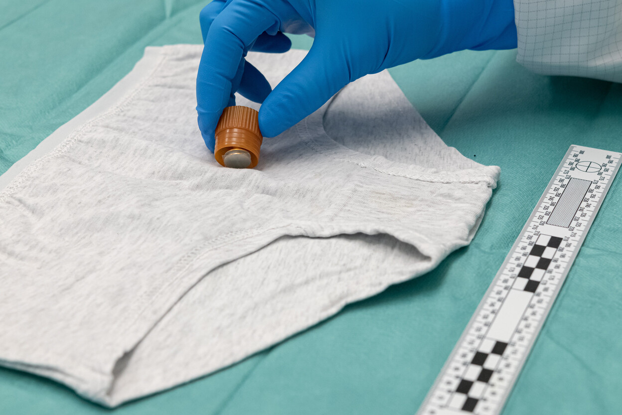 Grijze onderbroek op tafel met liniaal, onderzoeker bemonstert met stub