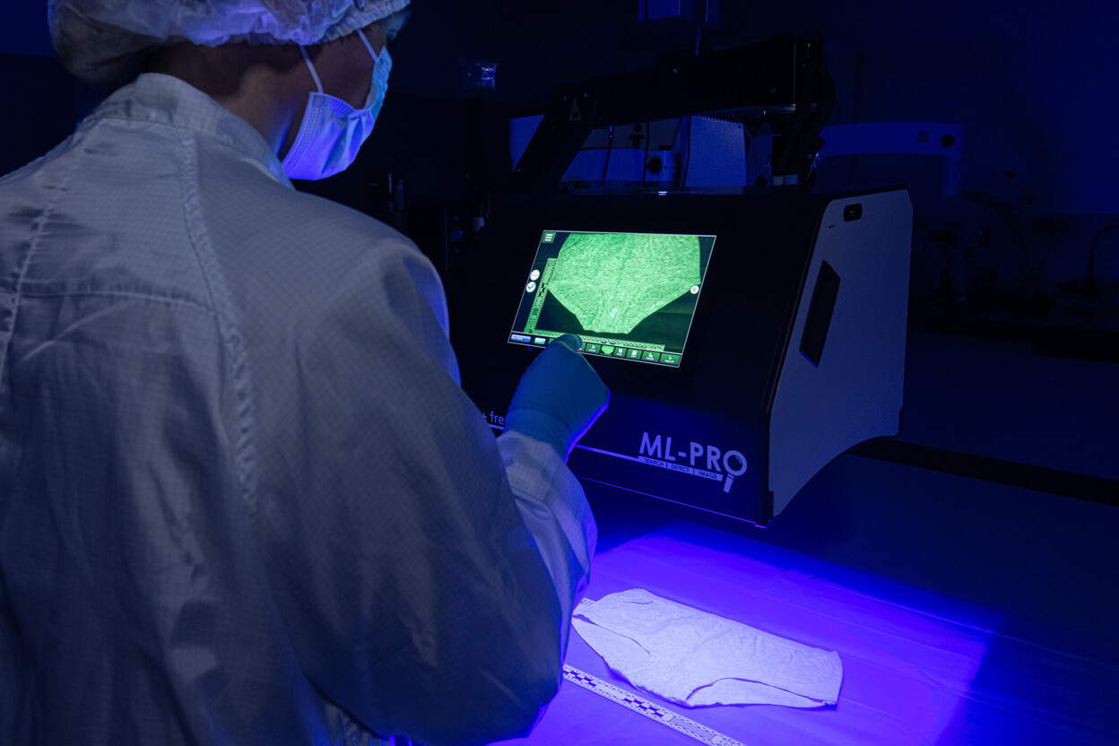 Onderzoeker bekijkt onderbroek met blauw licht in een donkere ruimte