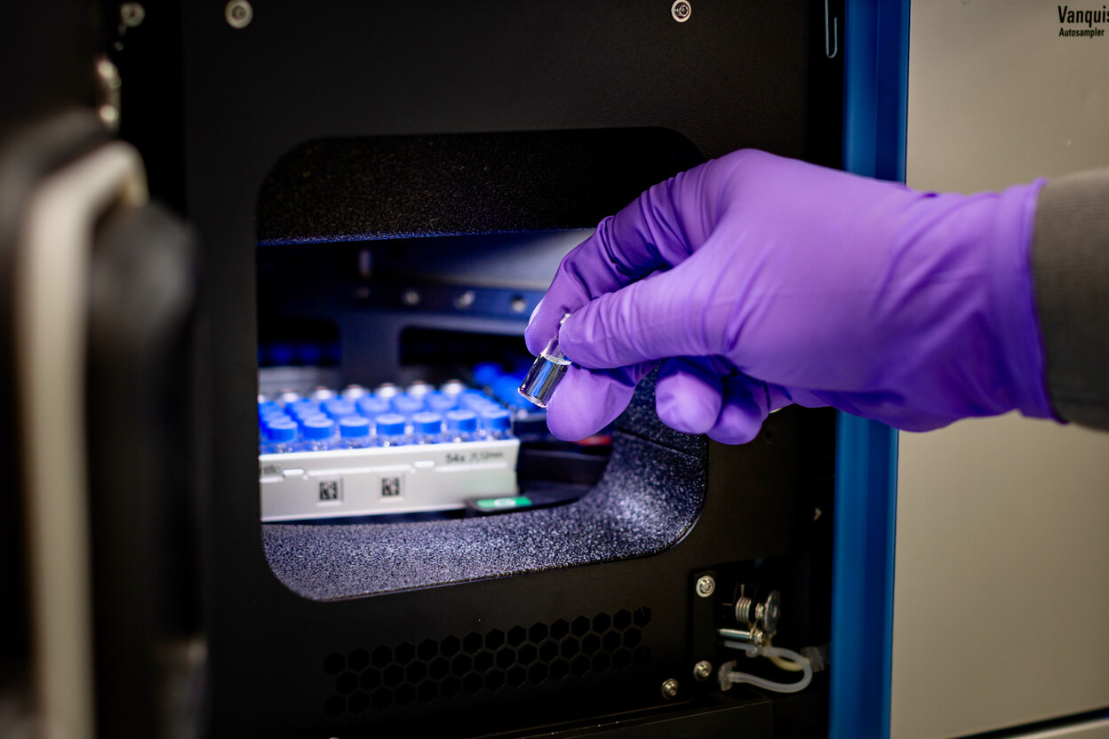 Onderzoeker plaatst glazen vaatje in apparaat