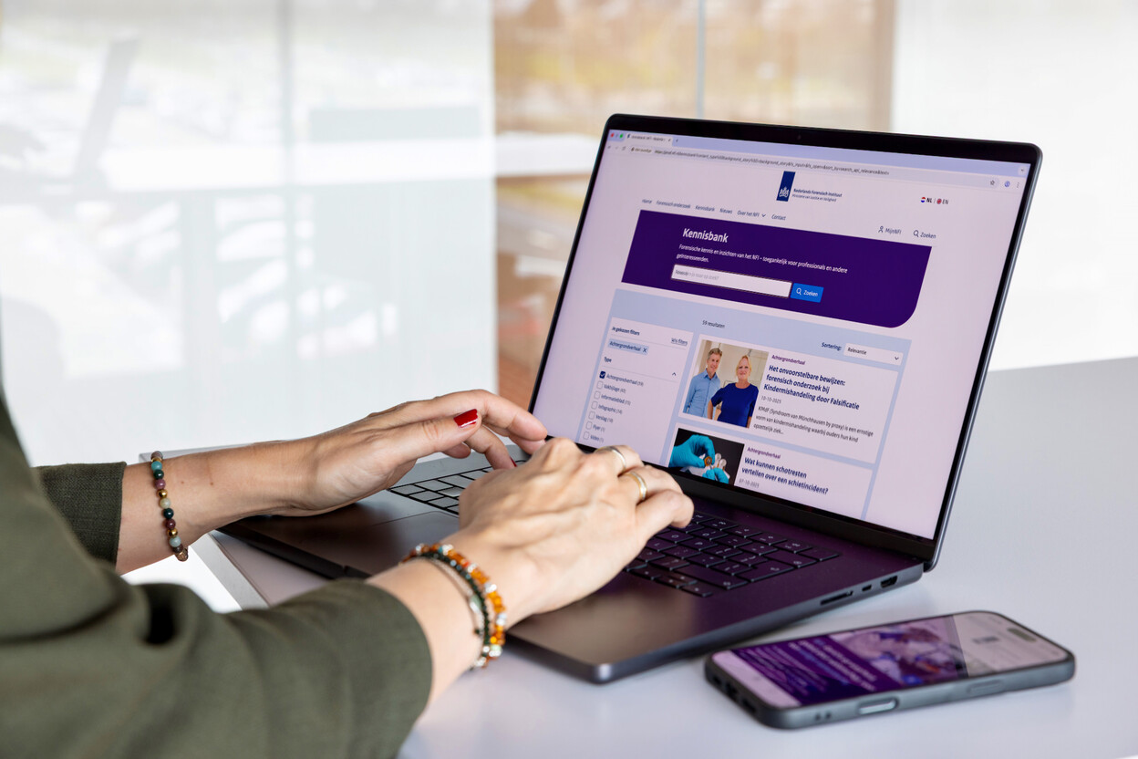 vrouw typt op toetsenbord laptop met NFI-website op het scherm