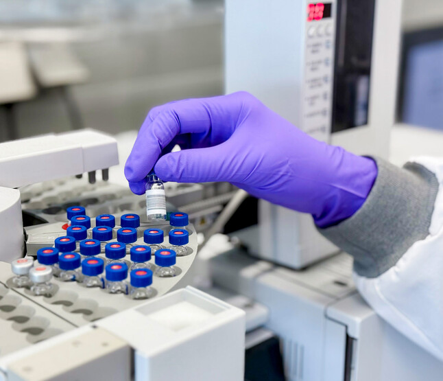 Close-up van hand onderzoeker die glazen vaatjes plaatst in apparatuur